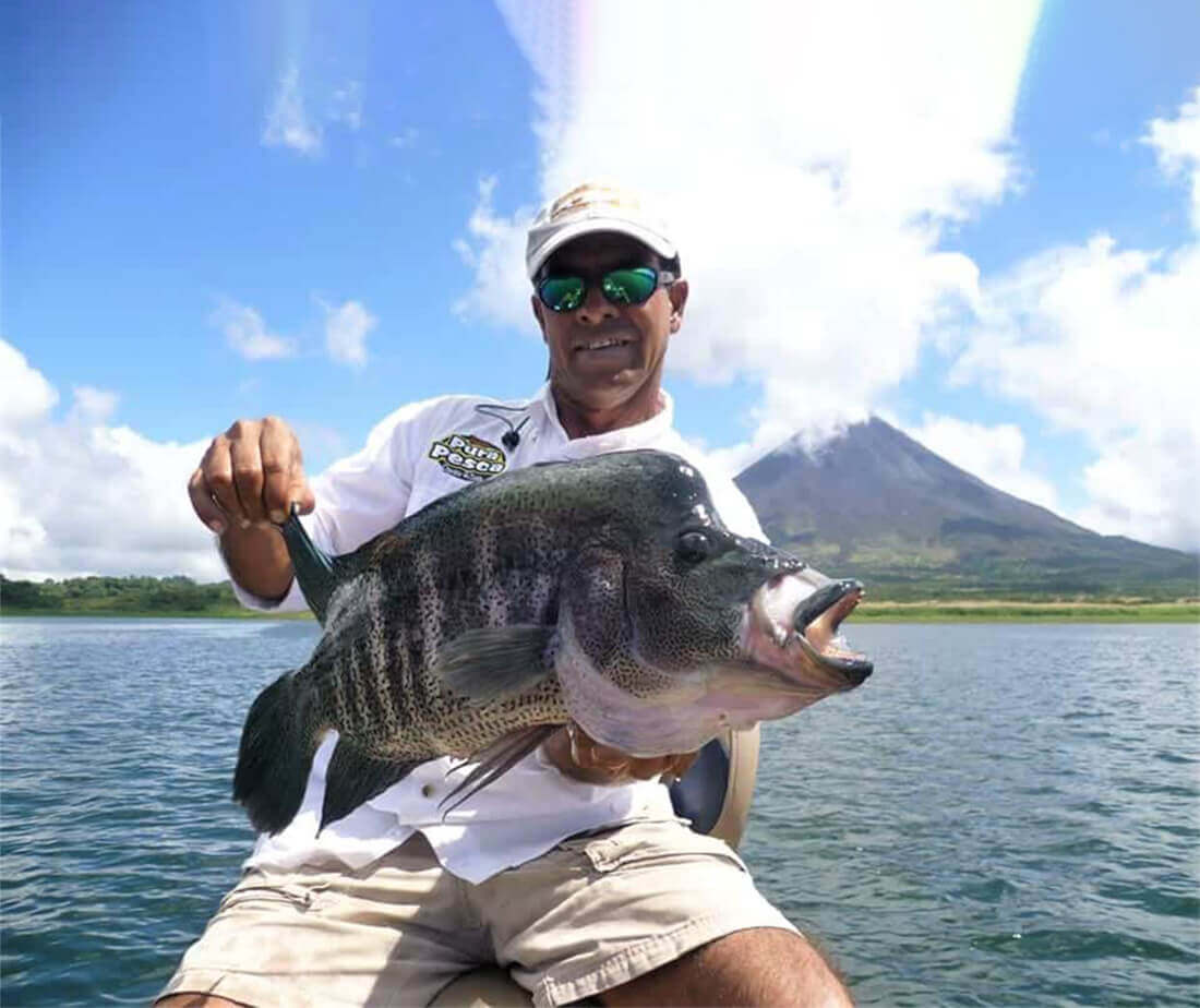 Legendary freshwater fishing guide, Tirsio, with a beautiful rainbow bass in front of the Arenal Volcano.